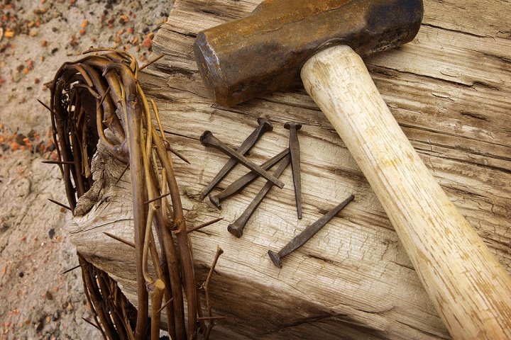 Photo illustration of a crown of thorns, old nails, hammer and wood beam.