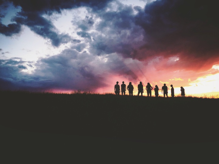 A group of people standing on top of a hill with the sun setting in the background.