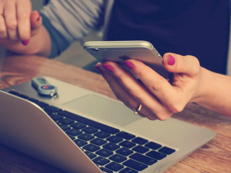 woman working on her computer and checking her phone