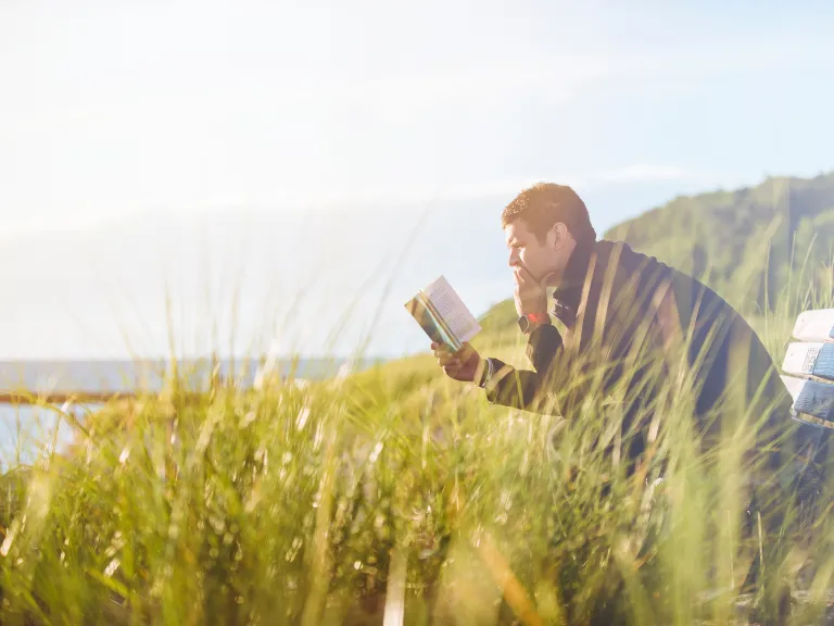 A man reading a Bible sitting on a park bench.