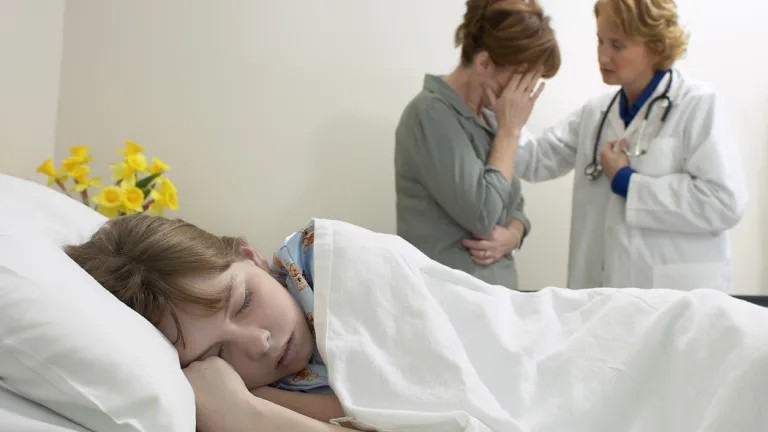A young child laying in bed with a mother and doctor in the background.