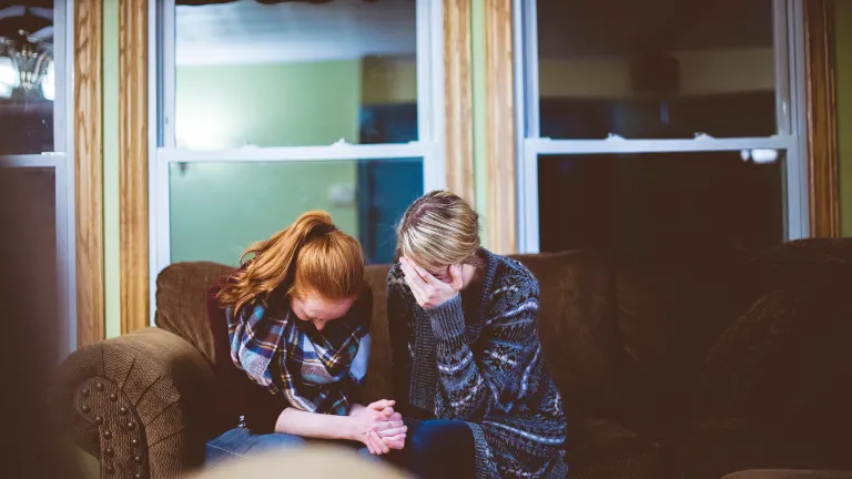 Two women sitting together on a couch crying.