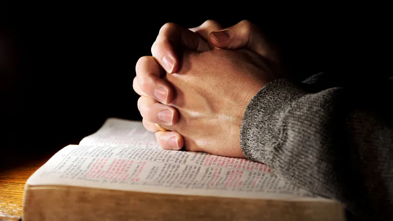 A man's hands clasped on top of a Bible.