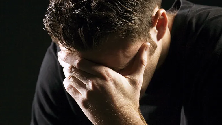 A man with his hand holding his head while looking down.