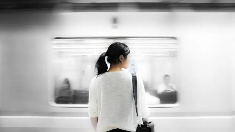 A woman standing has a train speeds by.