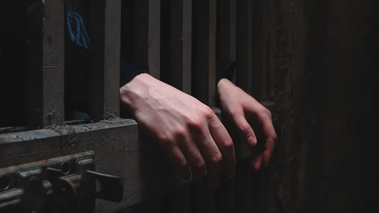 A person behind cell bars of a prison door.