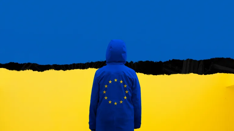 a person wearing a blue jacket with stars faces a torn Ukrainian flag
