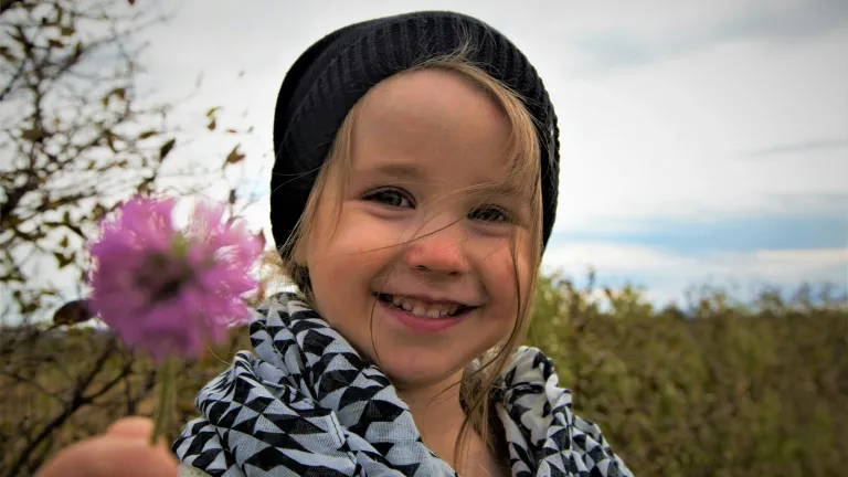 a little girl smiling and holding a flower