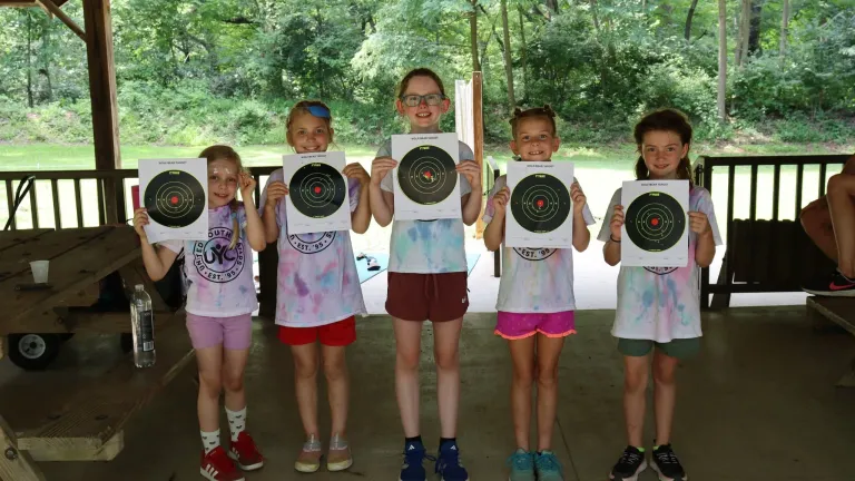 five girls holding up paper archery targets