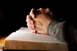 A man's hands clasped on top of a Bible.