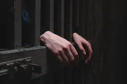 A person behind cell bars of a prison door.